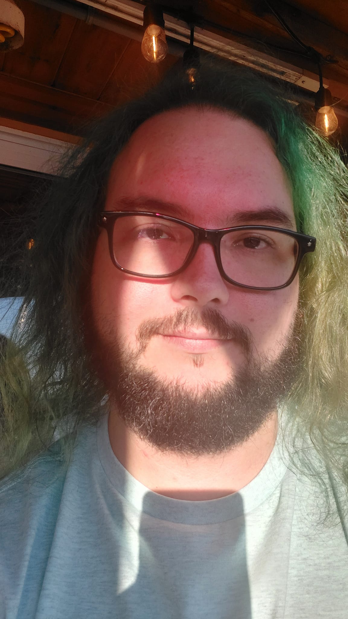 A man with green hair is sitting on a patio in the sunlight, Photo 4